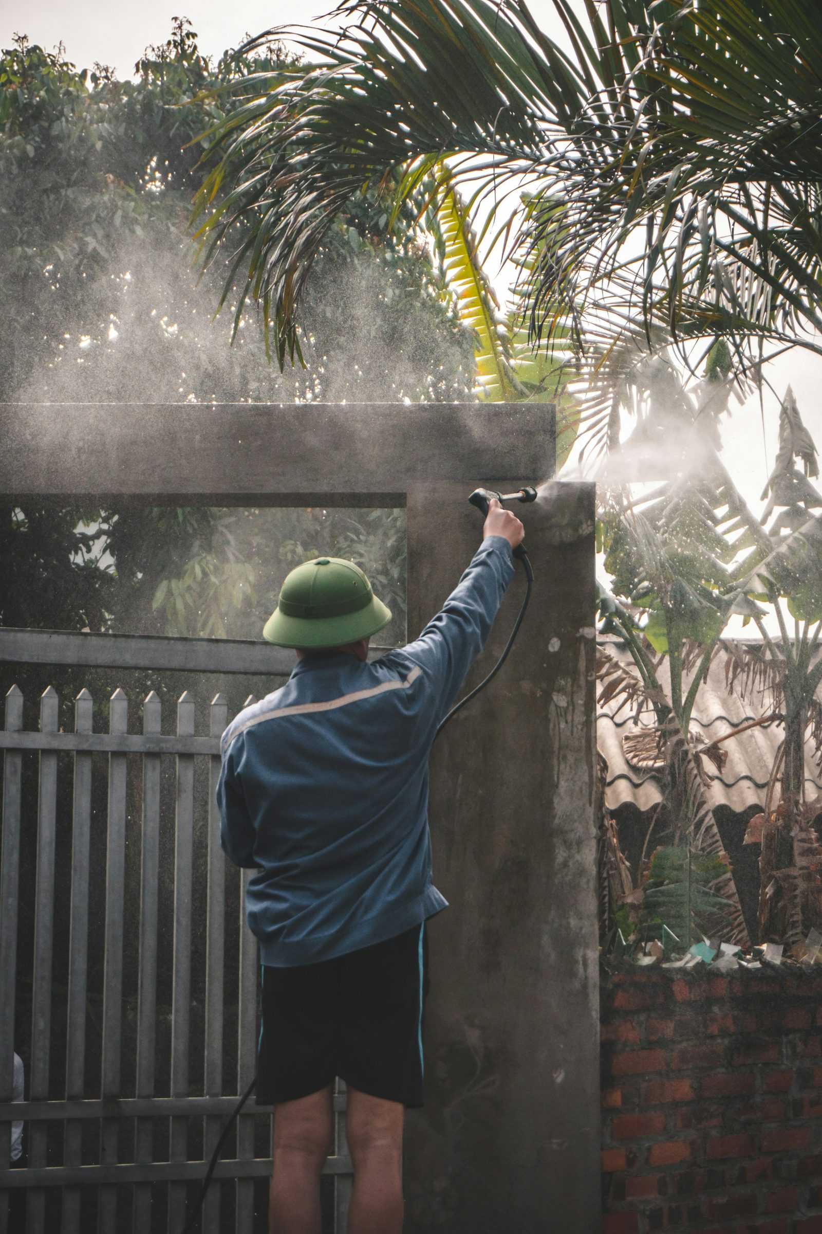 Person soft washing an exterior wall and gate with a spray wand